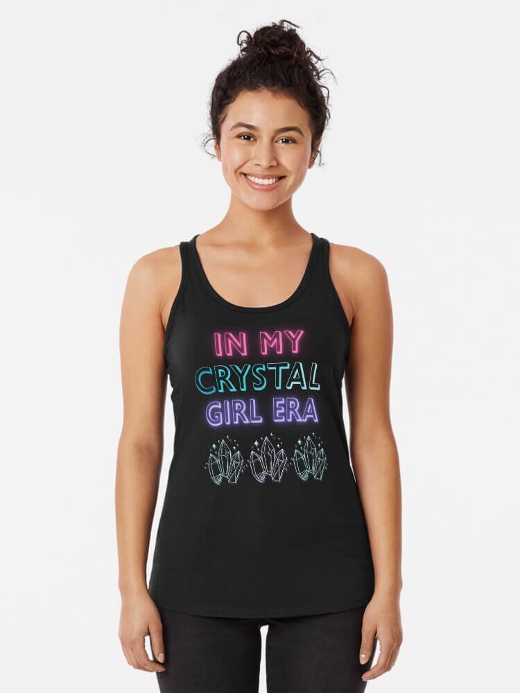 Woman wearing black racerback tank that reads ‘In My Crystal Girl Era’ in neon letters with crystal illustrations along the bottom.