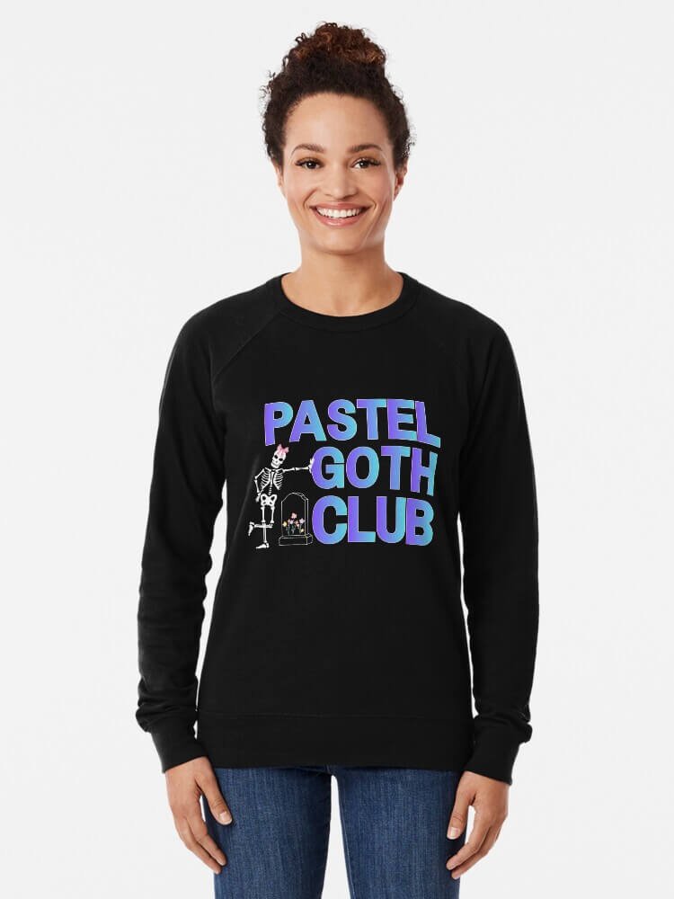 Person wearing a black lightweight sweatshirt that says ‘Pastel Goth Club’ in pastel gradient letters with a cute skeleton graphic