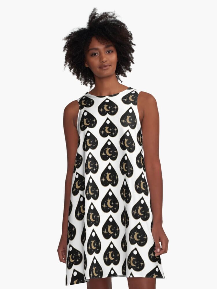 Front view of woman wearing white A-line dress with repeating black and gold planchette pattern featuring crescent moons and stars.