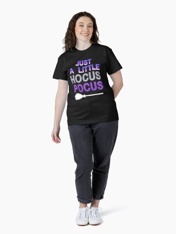 Person wearing a black classic t-shirt that says ‘Just A Little Hocus Pocus’ in purple and silver text with a white broom illustration, standing against a plain white background.