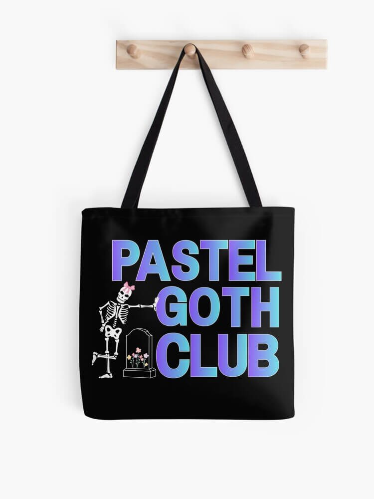 Black tote bag hanging on a wooden peg with large gradient text reading ‘Pastel Goth Club’ and a cute skeleton by a small flowered gravestone