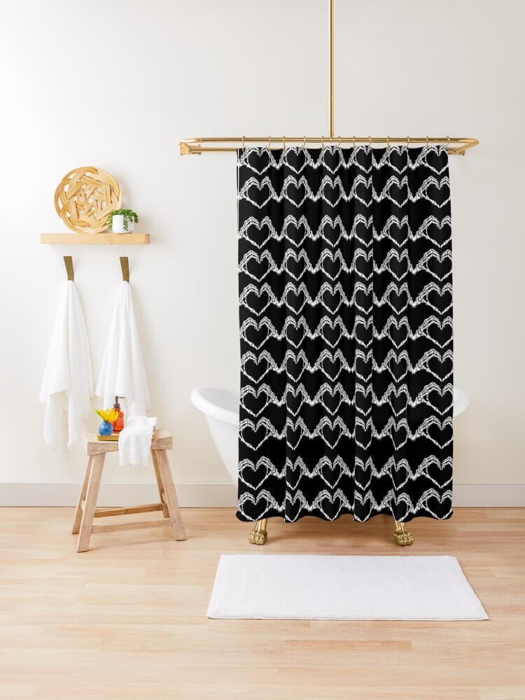 Black shower curtain with repeating white skeleton hand hearts hanging next to a clawfoot tub in a bright bathroom