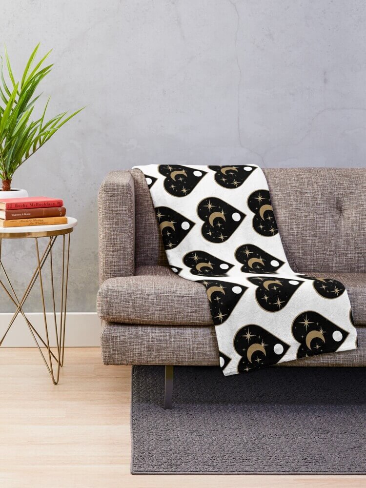 Golden Planchette blanket draped over a grey sofa, showing repeating moon and star ouija planchette design in a modern living room.